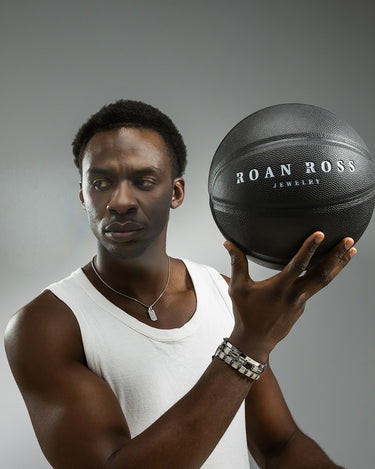 Man met een basketbal en een zilveren ketting, vertegenwoordigt luxe heren sieraden van Roan Ross.